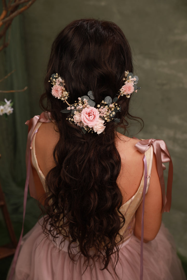 Woman with long, wavy hair adorned with floral hair accessories and pink ribbons against a green background.