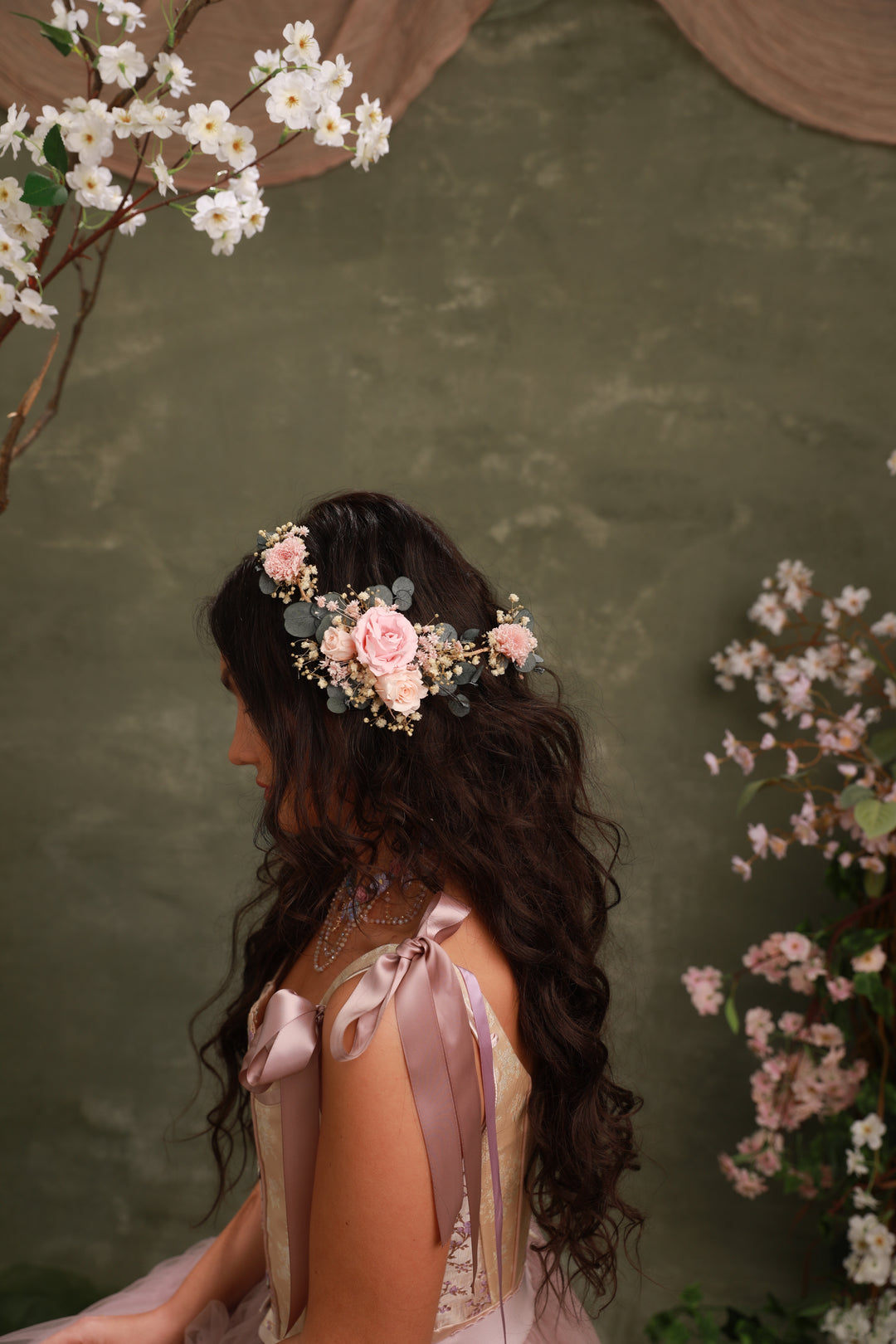 Woman with floral hairpiece with preserved roses and eucalyptus and ribbons against a green background with floral elements