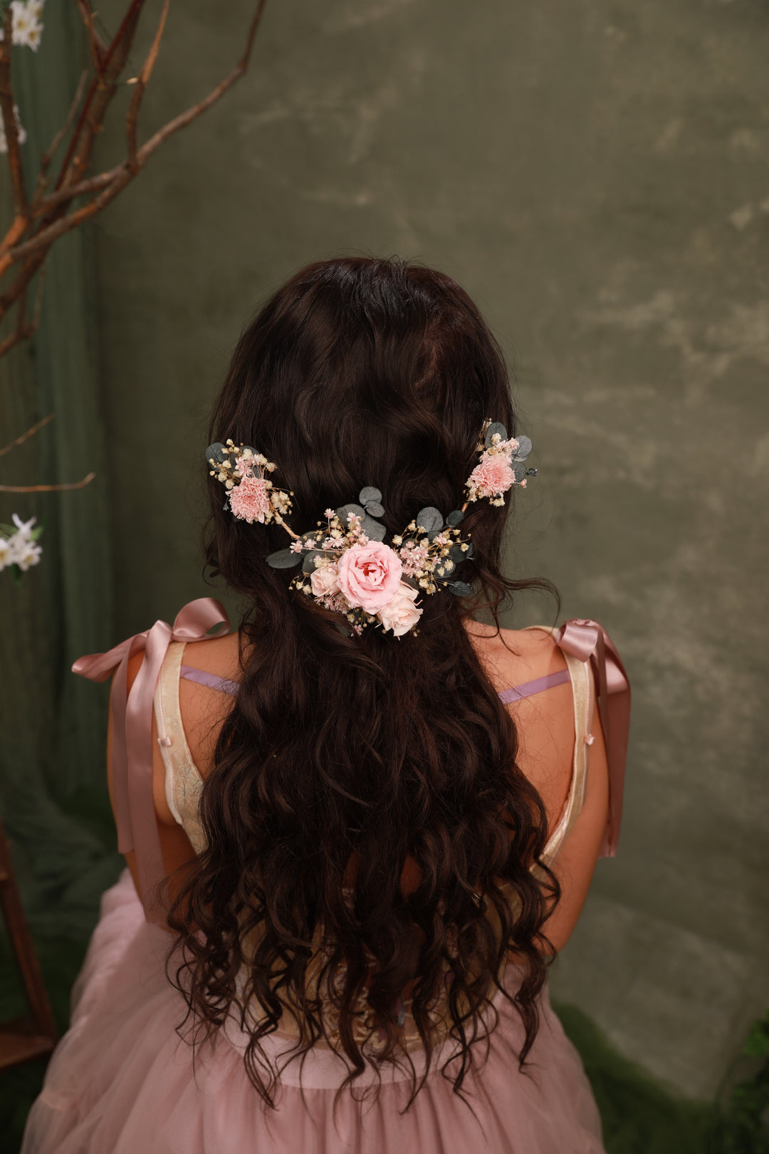 Person with floral hair accessory and pink dress against a green background