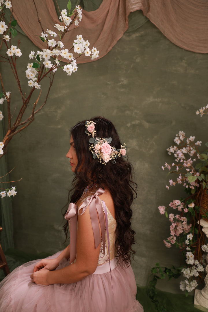 Woman in a pink dress with floral headpiece sitting against a green wall with cherry blossom branches.