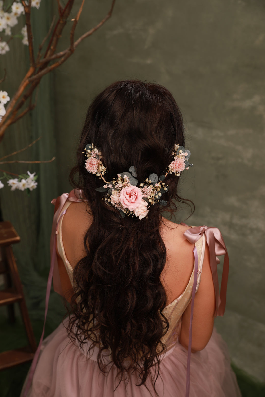 Woman with long, wavy hair adorned with floral hair accessories against a green background