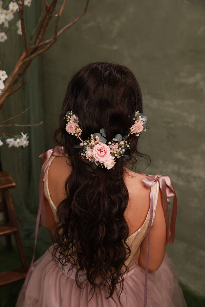 Woman with long, wavy hair adorned with floral hair accessories against a green background