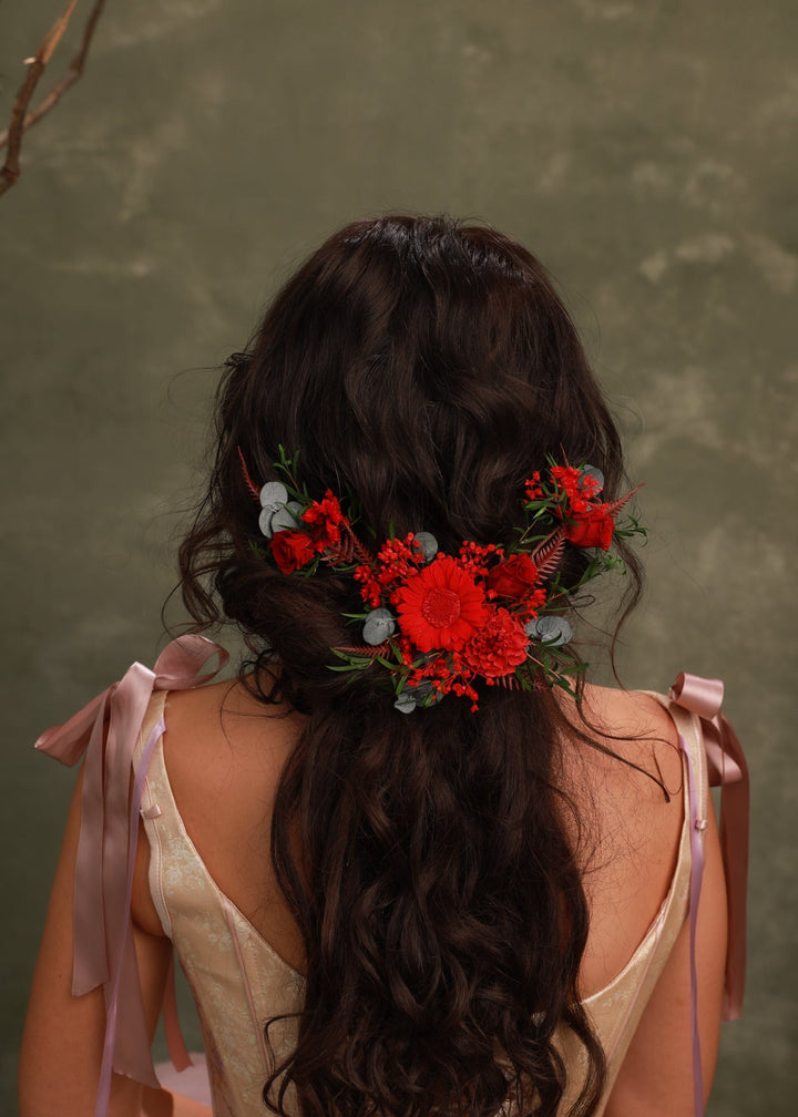 Woman with long dark hair adorned with red flowers and greenery against a green background