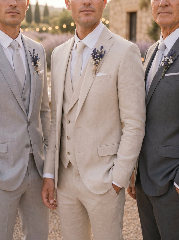 Three men in suits standing together outdoors with a stone building and trees in the background with natural boutonnieres