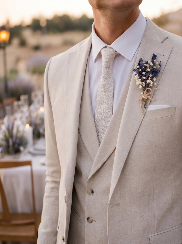 Man wearing a beige suit with a floral boutonniere at an outdoor event.