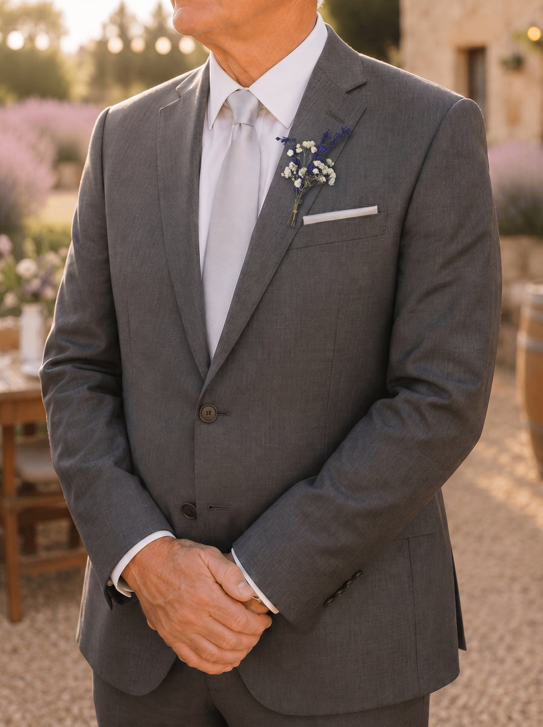 Man wearing a gray suit with a white shirt and tie, natural boutonniere, standing outdoors.