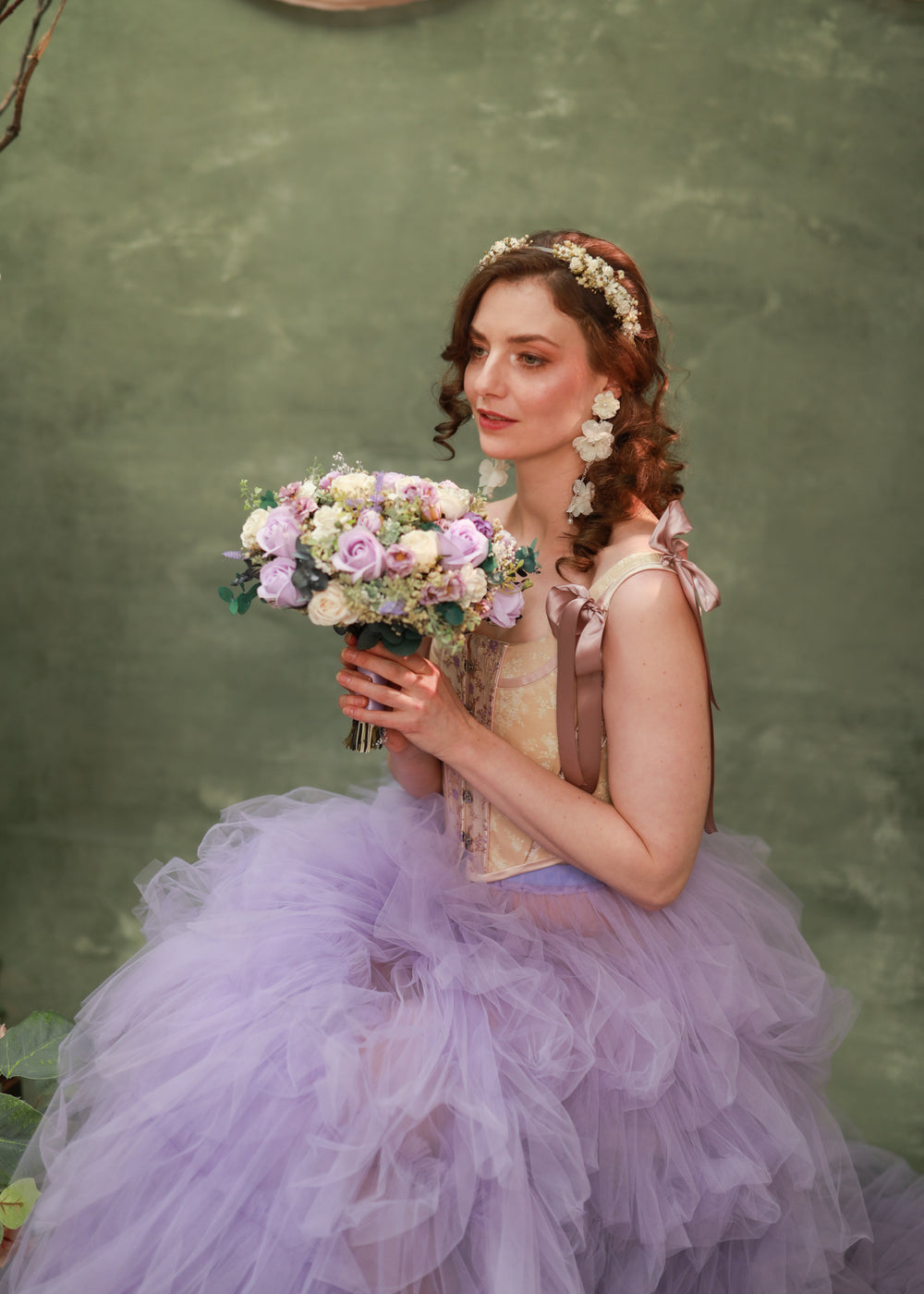 Woman in a lavender dress holding a round bouquet of flowers against a green background