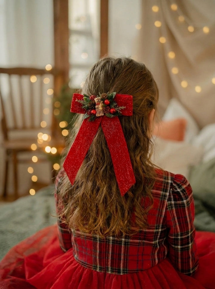A child viewed from behind wearing a red plaid dress and a large red glitter bow with holly and berries in their hair, seated in a softly lit room with warm string lights in the background.