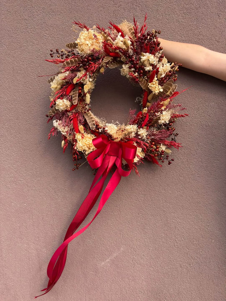 Measuring approximately 45 cm in diameter, this wreath creates a beautiful focal point on an interior door or wall. Imagine it above a wooden console, bringing colour to the everyday ritual of coming home. Its red and cream palette pairs beautifully with warm wood, woven textiles and simple seasonal decorations.