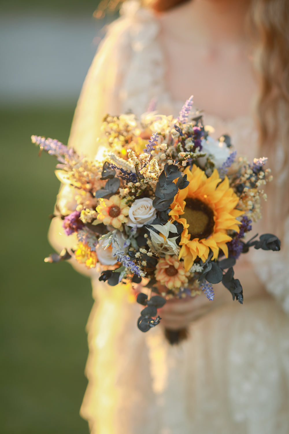 Bouquet of sunflowers and other flowers held by a person in a blurred outdoor setting