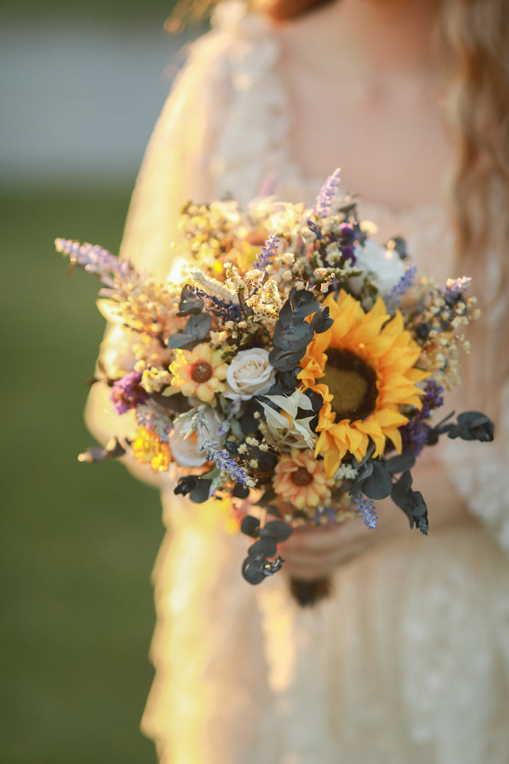 Bouquet of sunflowers and other flowers held by a person in a blurred outdoor setting