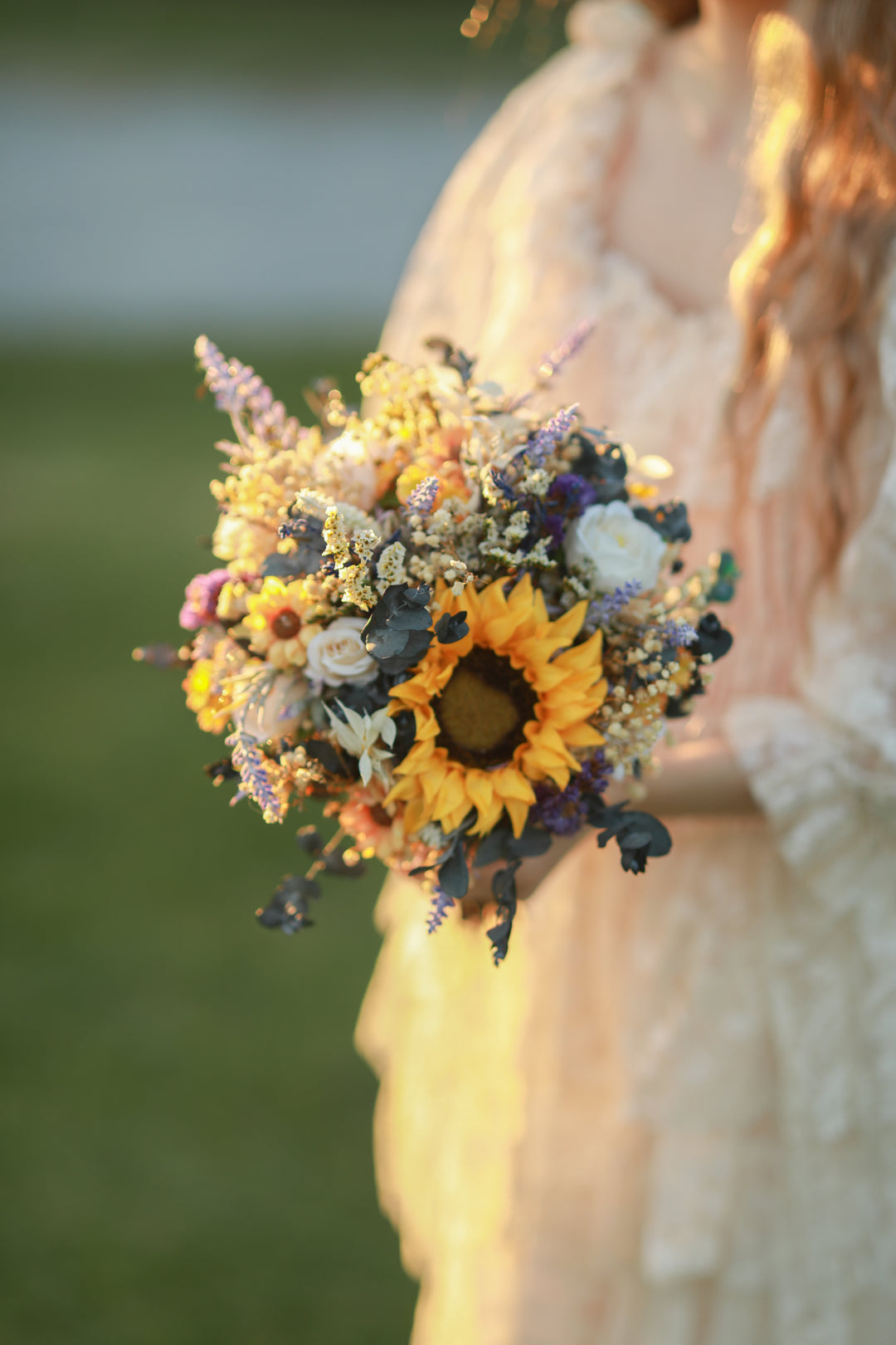 Bouquet of sunflowers and other flowers held by a person with a blurred natural background