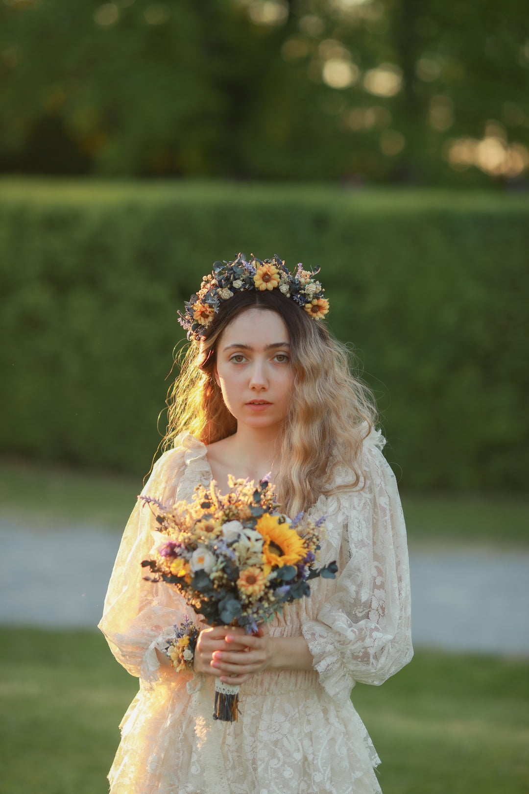 Woman in a white dress with a floral headpiece and bouquet standing outdoors.