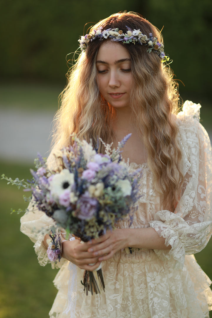 Woman in a lace dress holding a bouquet of flowers with a floral headband.