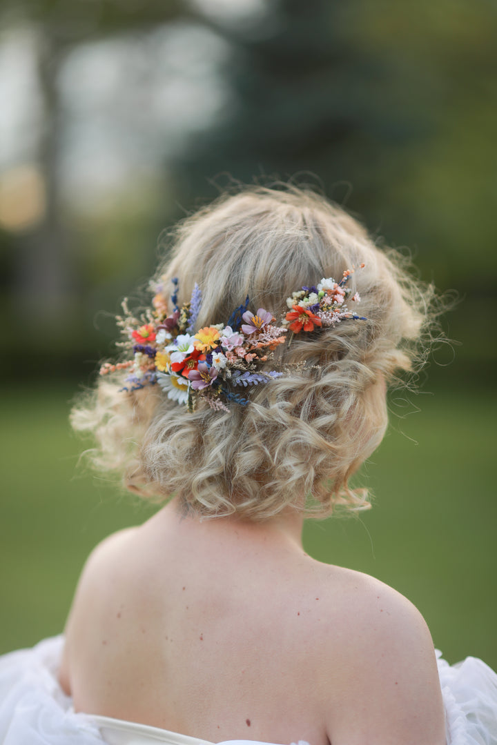 Person with curly hair adorned with a floral headpiece in meadow design  against a blurred natural background