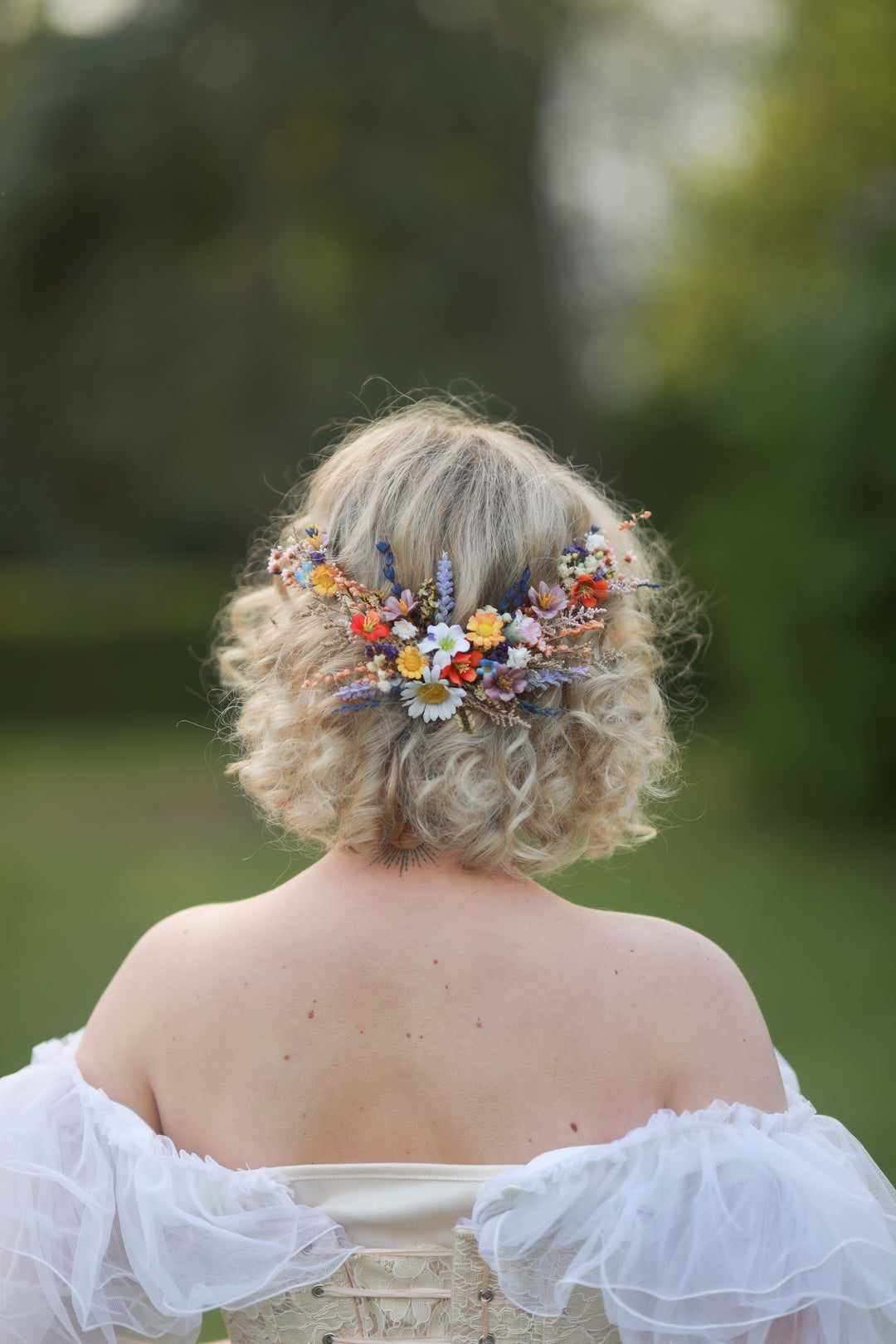 Person with floral hairpiece and white off-shoulder top in a natural setting