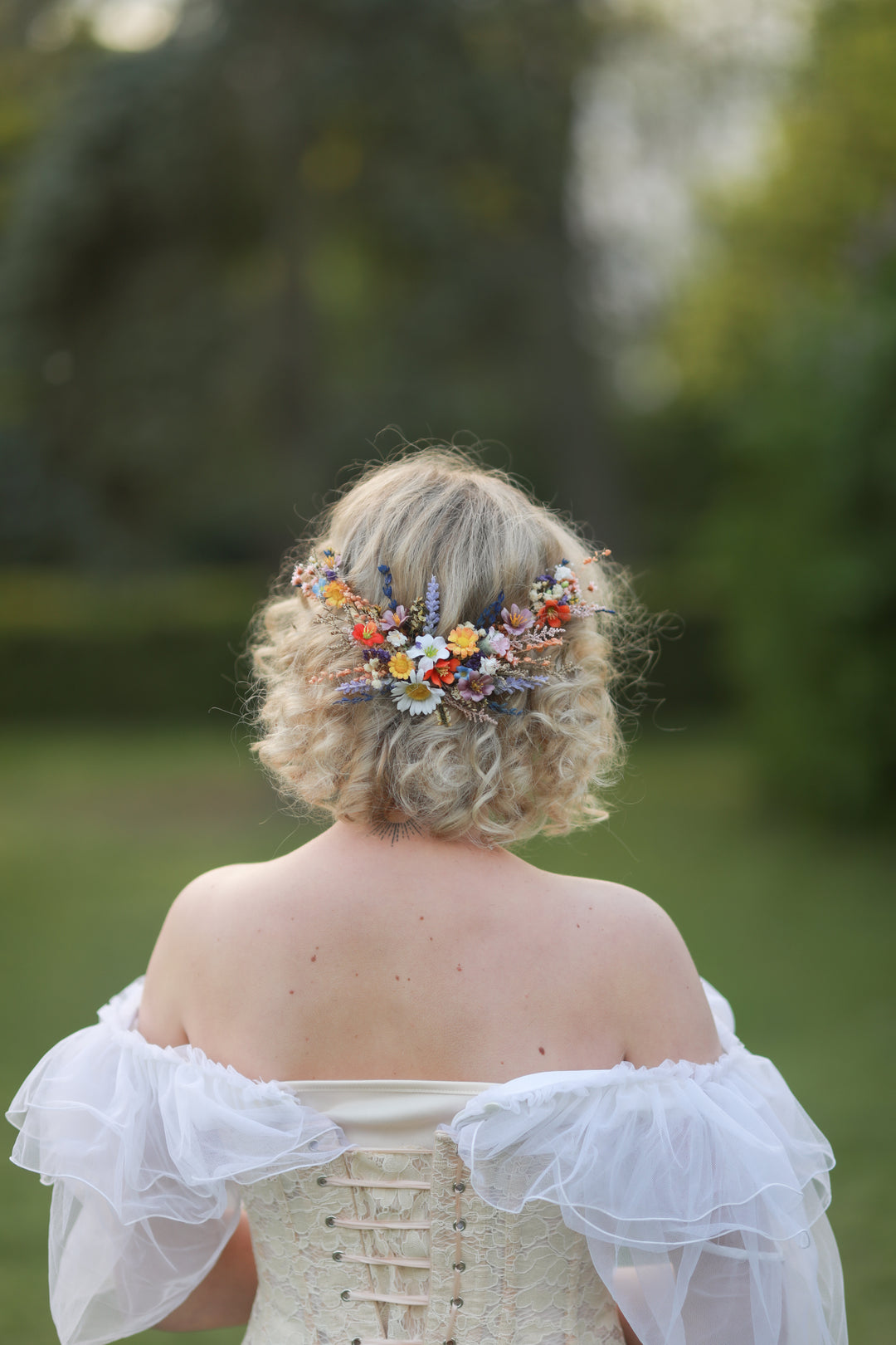 Person with floral hairpiece wearing a white off-shoulder dress in a natural setting