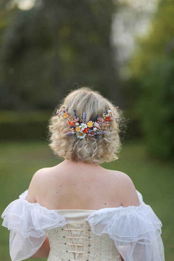 Person with floral hairpiece wearing a white off-shoulder dress in a natural setting