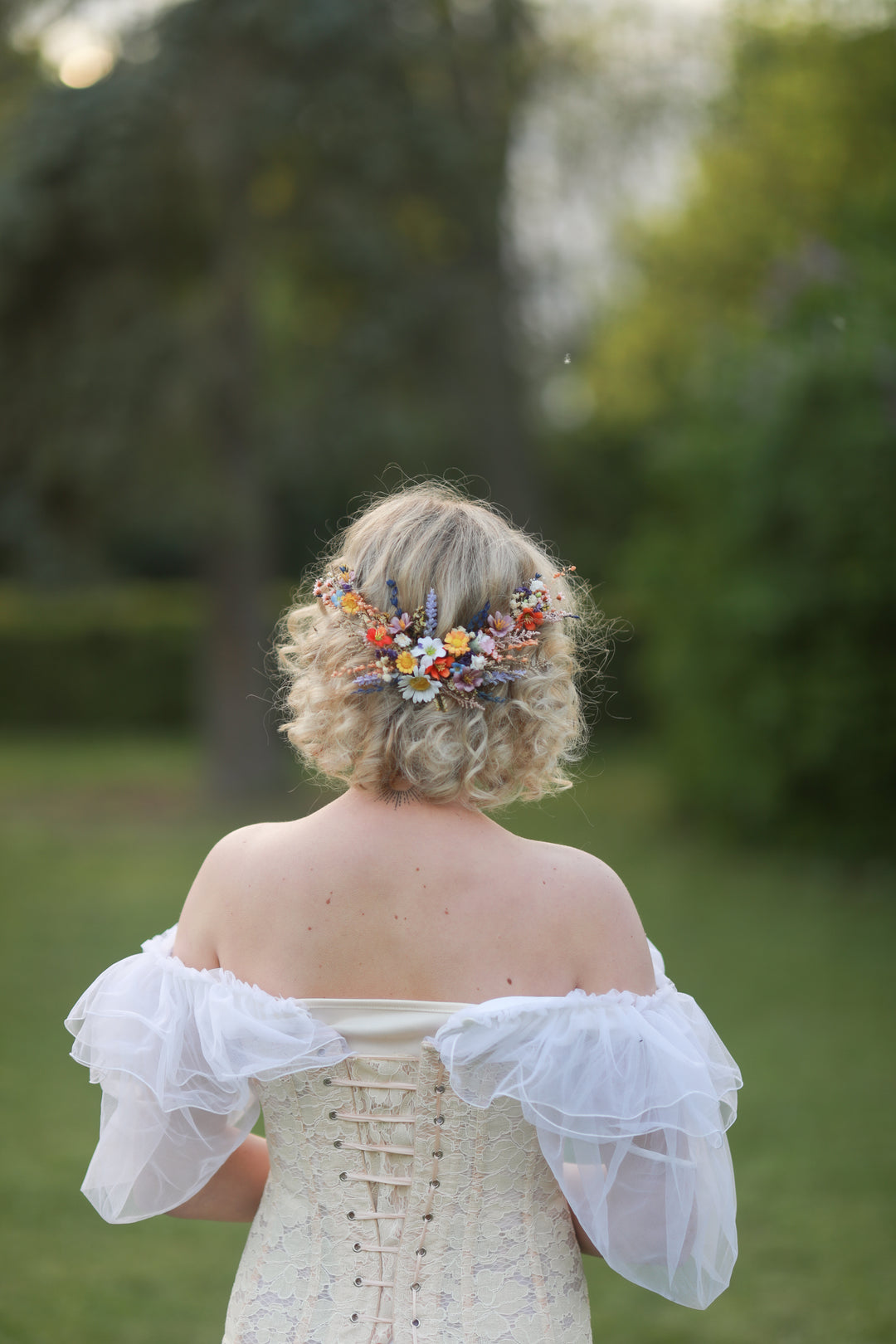 Bride with floral hairpiece with wild flowers  wearing a white off-shoulder dress in a natural setting