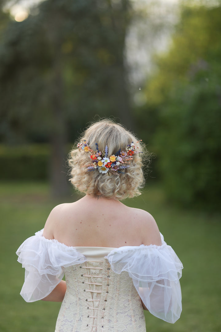 Bride with floral hairpiece with wild flowers  wearing a white off-shoulder dress in a natural setting