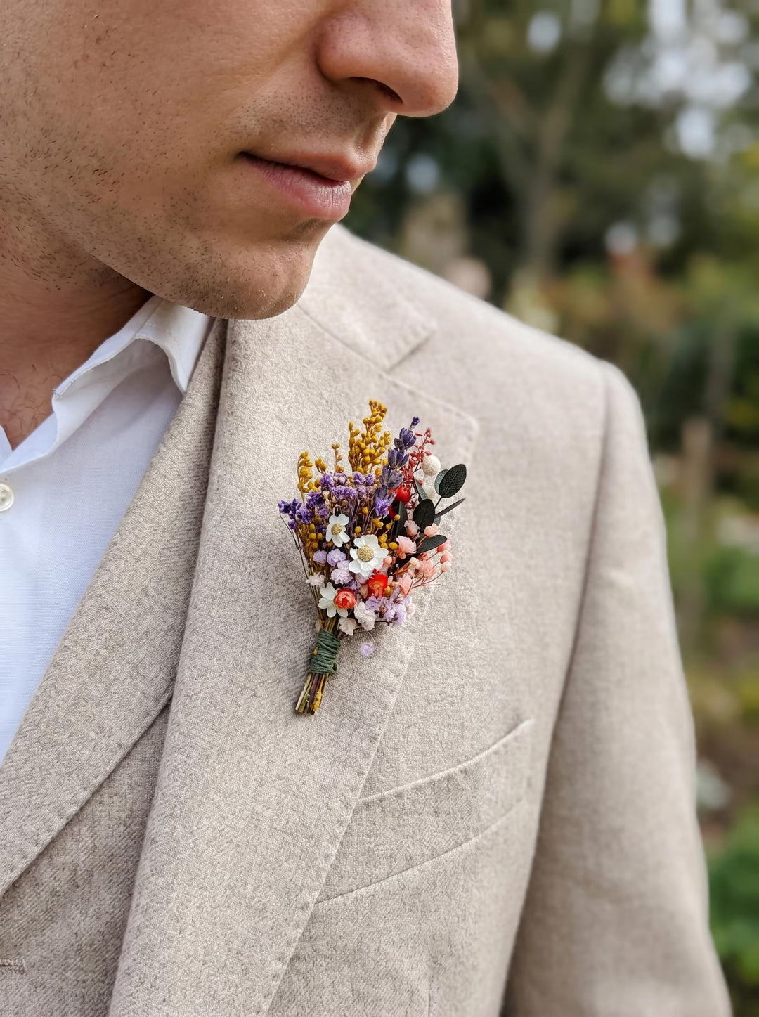 Man wearing a beige suit with a colorful floral boutonniere outdoors.