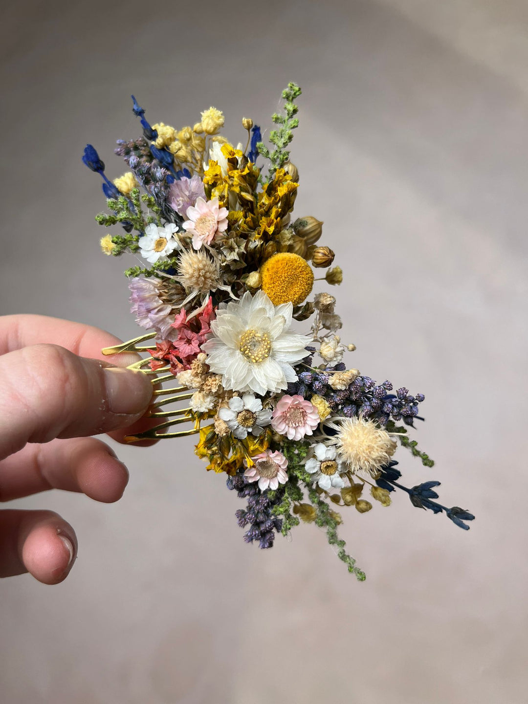 Hand holding a floral hair comb with dried flowers against a neutral background