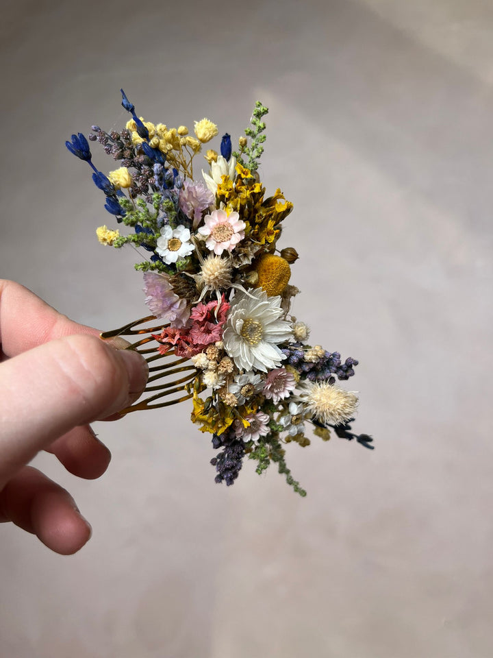 Hair comb with dried flowers held by a hand against a neutral background