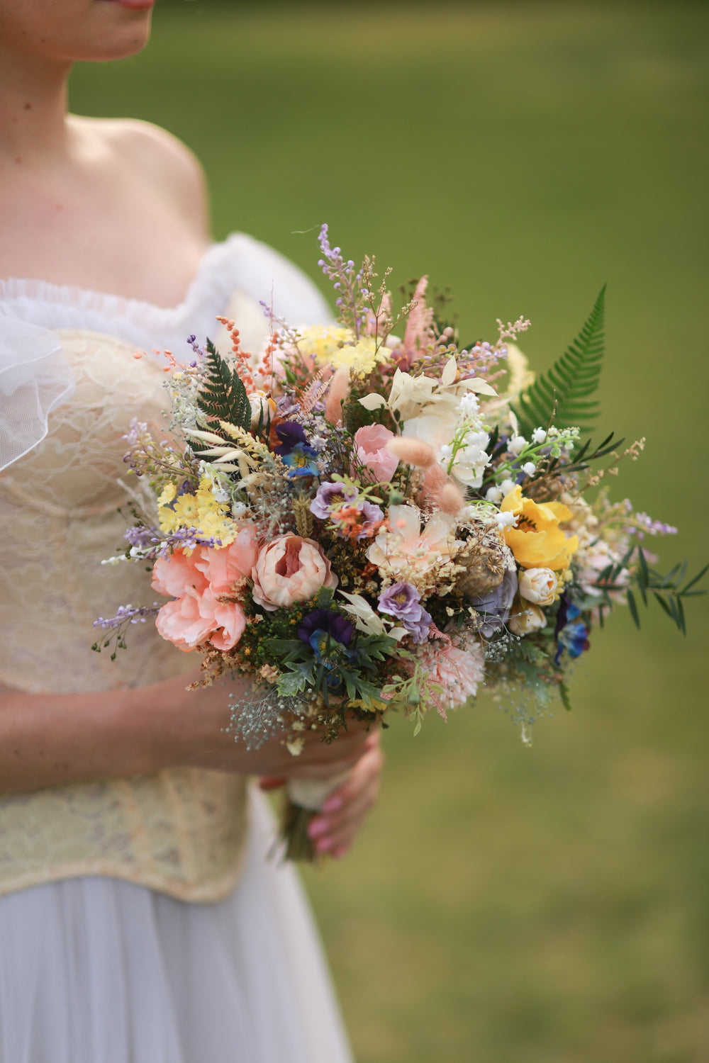 Bouquet of flowers held by a person in a white dress against a blurred green background