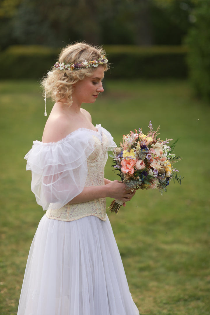 Woman in a white dress holding a bouquet of flowers outdoors.