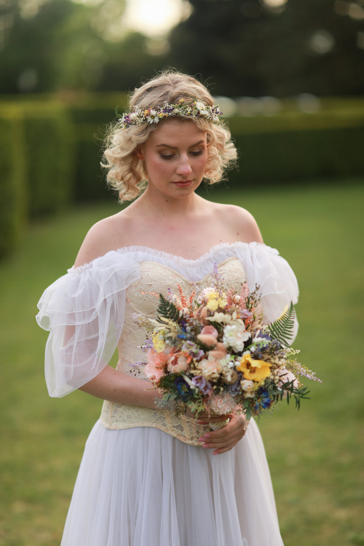 Woman in a white dress holding a wildflowers colorful  bouquet of flowers outdoors.
