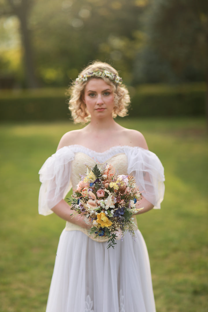 Woman in a white dress holding a bouquet of wild colorful flowers in a park setting