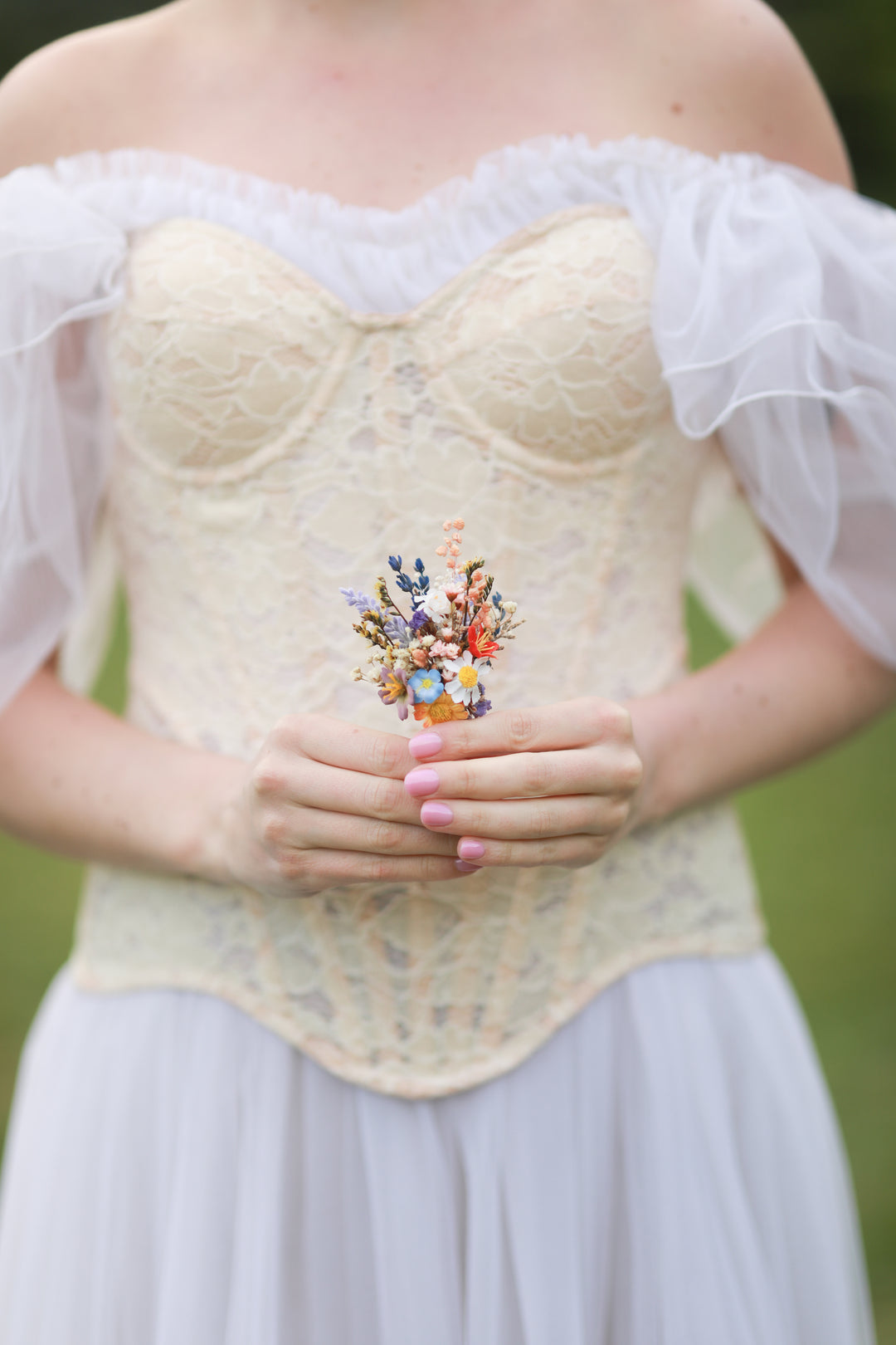 Woman wearing a lace corset and holding a colorful boutonniere against a blurred green background