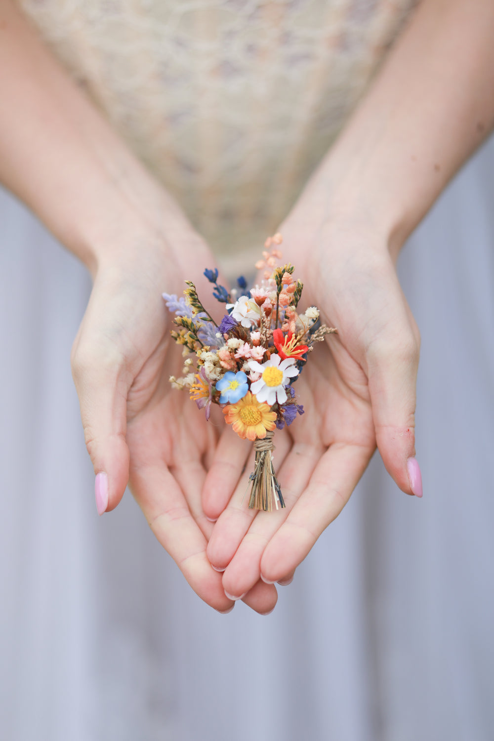 Hands holding a small boutonniere of colorful flowers against a blurred background