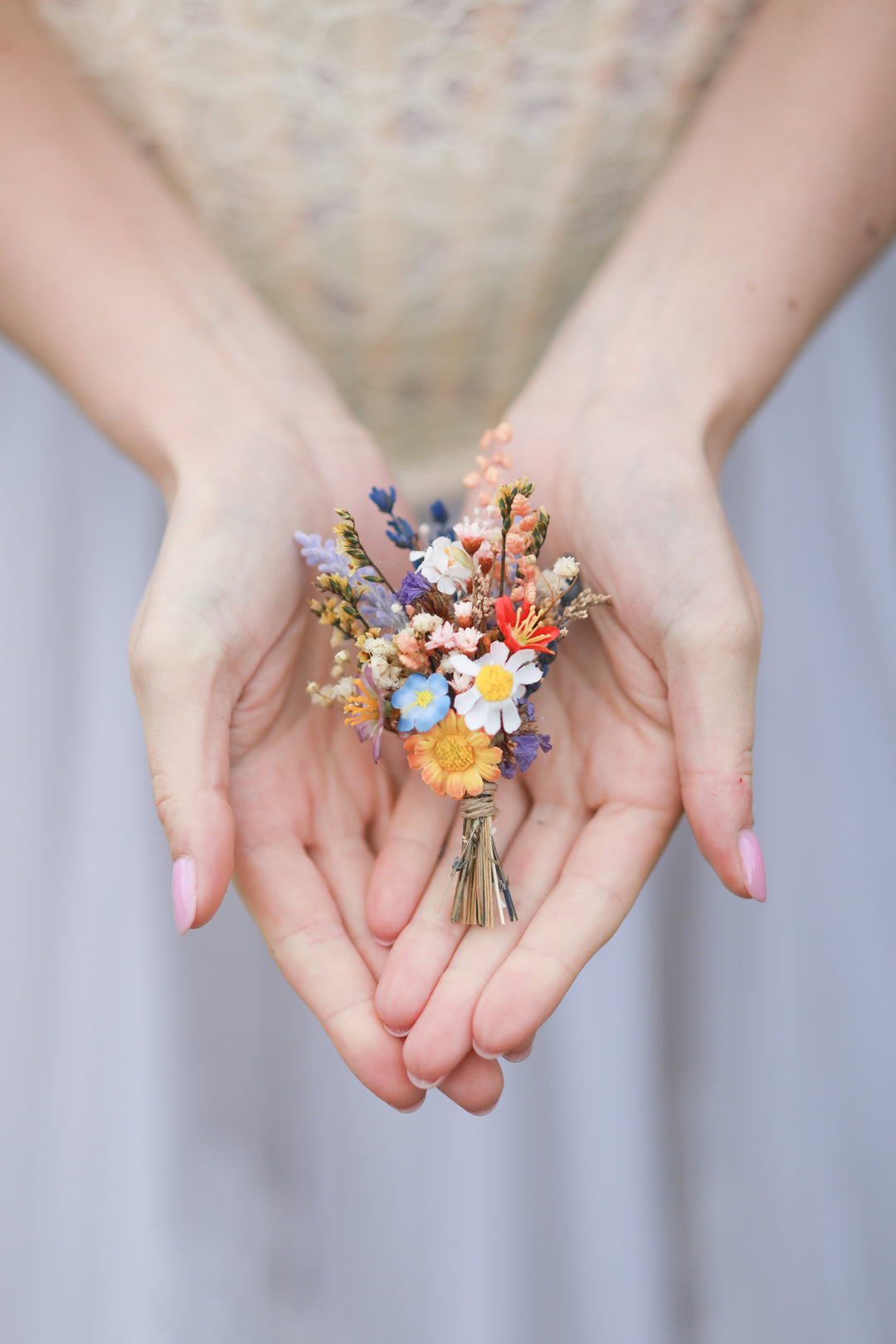 Hands holding a small boutonniere of colorful flowers against a blurred background