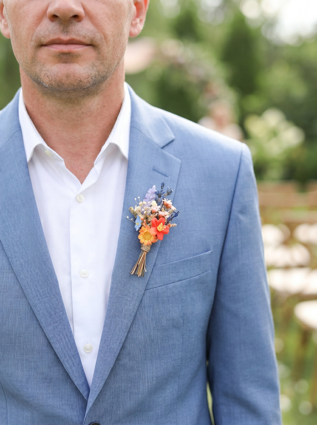 Man wearing a light blue suit with a colorful boutonniere outdoors.