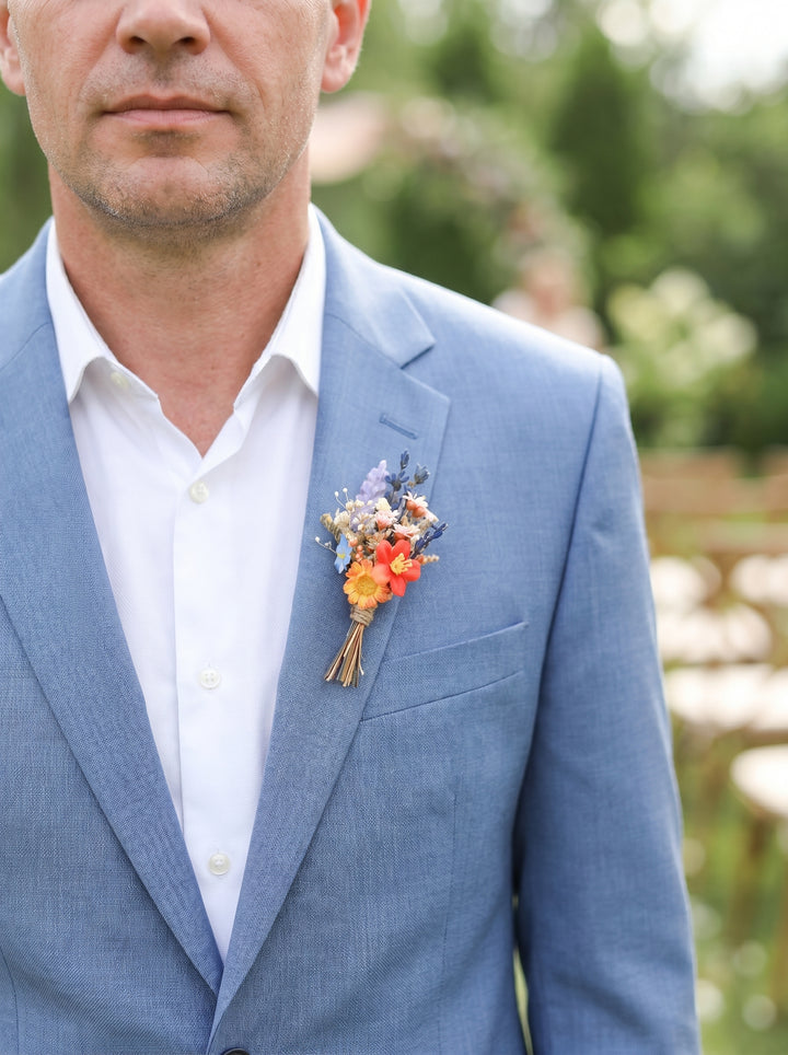 Man wearing a light blue suit with a colorful boutonniere outdoors.