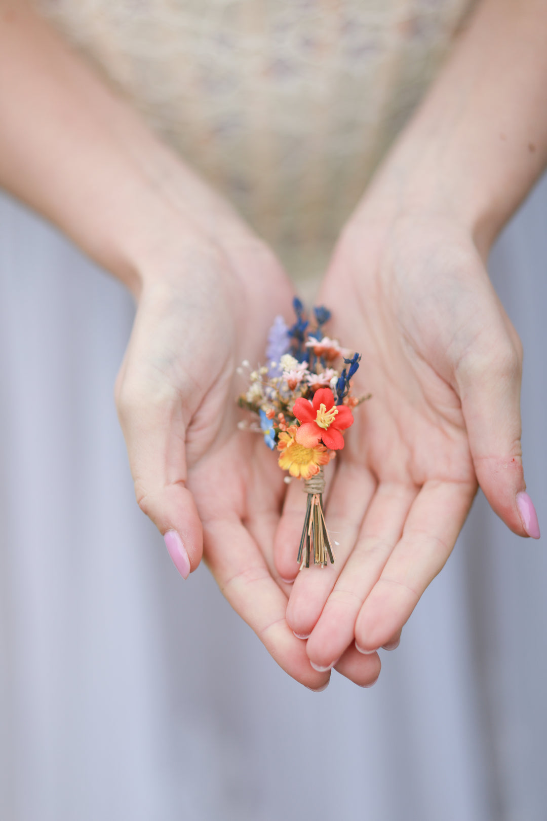 Two hands holding a small wedding boutonniere of flowers against a blurred background
