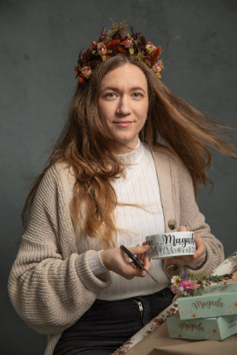 Woman with a floral crown holding a product labeled 'Magaela' against a dark background